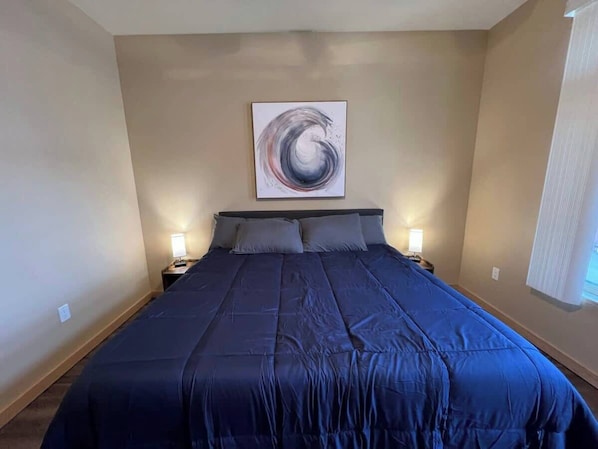 A bedroom with a large bed, a wall-mounted abstract painting, and two bedside lamps.
