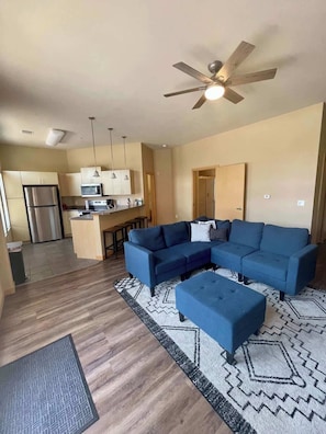 A modern living room with a sectional sofa, ottoman, and a ceiling fan.