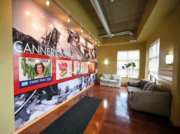 A lobby with a wall displaying vintage advertisements, a sofa, a potted plant, and a window with blinds.