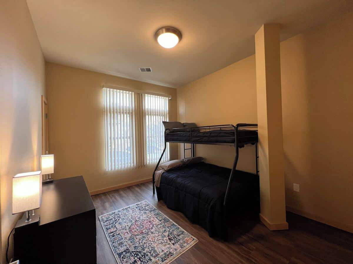 Ein Zimmer mit einem Etagenbett, einem Schreibtisch mit Lampe, einem Teppich und einem Fenster mit Jalousien.