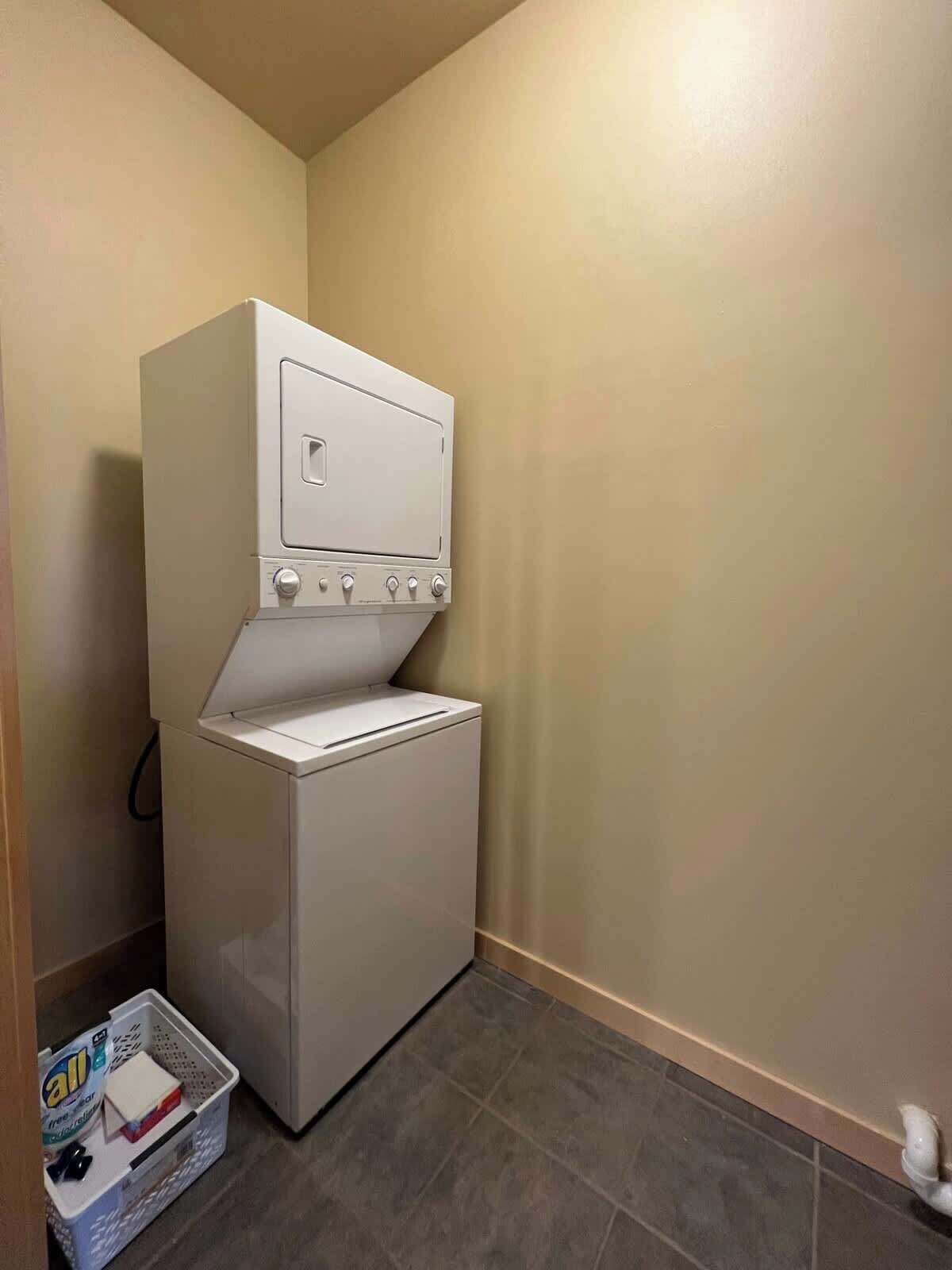 A compact laundry room with a washer and dryer, a small storage bin, and a tiled floor.