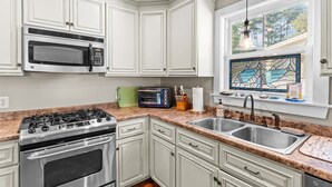 Una cocina con armarios blancos, estufa de acero inoxidable, microondas, tostadora y ventana con un vitral.