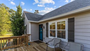 Una casa con terraza de madera, puerta azul y ventana con contraventanas.
