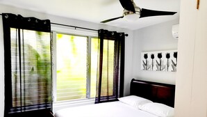 Quarto com cama, ventilador de teto e janela com cortinas.