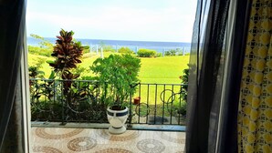 Uma varanda com chão de azulejos, um vaso de planta e vista para uma área gramada e o mar.