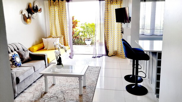 Sala de estar com sofá, mesa de centro e TV fixada na parede.