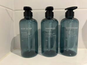 Three bottles of body soap, shampoo, and conditioner on a white shelf.