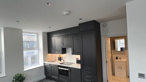 A modern kitchen with dark cabinetry, a built-in oven, and a window providing natural light. - Stylish Central Studio Apartment Modern Luxury (Brighton)
