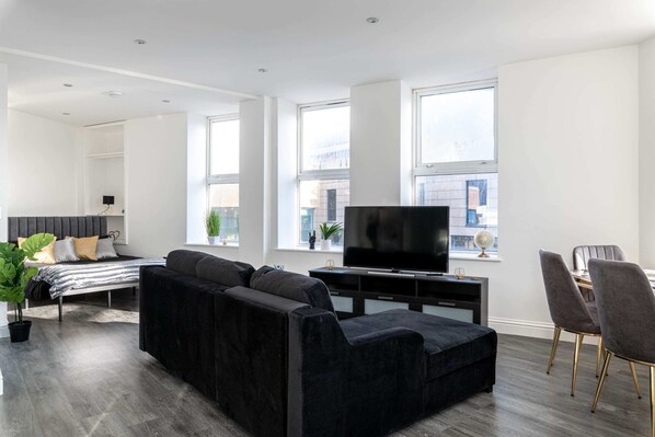 Un salon moderne avec un canapé noir, un téléviseur à écran plat et un coin repas avec des chaises.