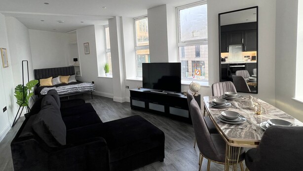 A modern living room with a sofa, TV, dining table, and chairs. - Stylish Central Studio Apartment Modern Luxury (Brighton)