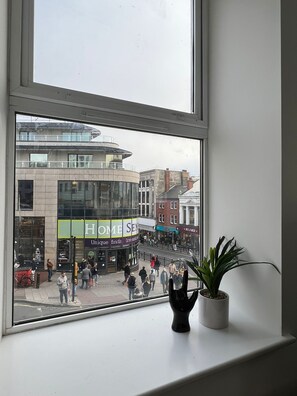 Une vue depuis une fenêtre donnant sur une rue animée, bordée de boutiques et fréquentée par des piétons.