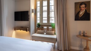 Hotelkamer met een bed, nachtkastje, een aan de muur bevestigde televisie, raam met gordijnen en een schilderij.