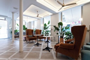 A spacious lobby with modern furniture, large windows, and potted plants. - Malabar by Petit Palace Anteriormente Icon Malabar (Málaga)