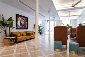 A spacious lobby with a yellow sofa, blue ottomans, and a large abstract painting on the wall. - Malabar by Petit Palace Anteriormente Icon Malabar (Málaga)