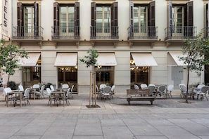 An outdoor cafe area with tables and chairs, a wooden bench, and a small tree. - Malabar by Petit Palace Anteriormente Icon Malabar (Málaga)