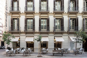 A building with multiple balconies, outdoor seating with tables and chairs, and awnings over the entrance. - Malabar by Petit Palace Anteriormente Icon Malabar (Málaga)