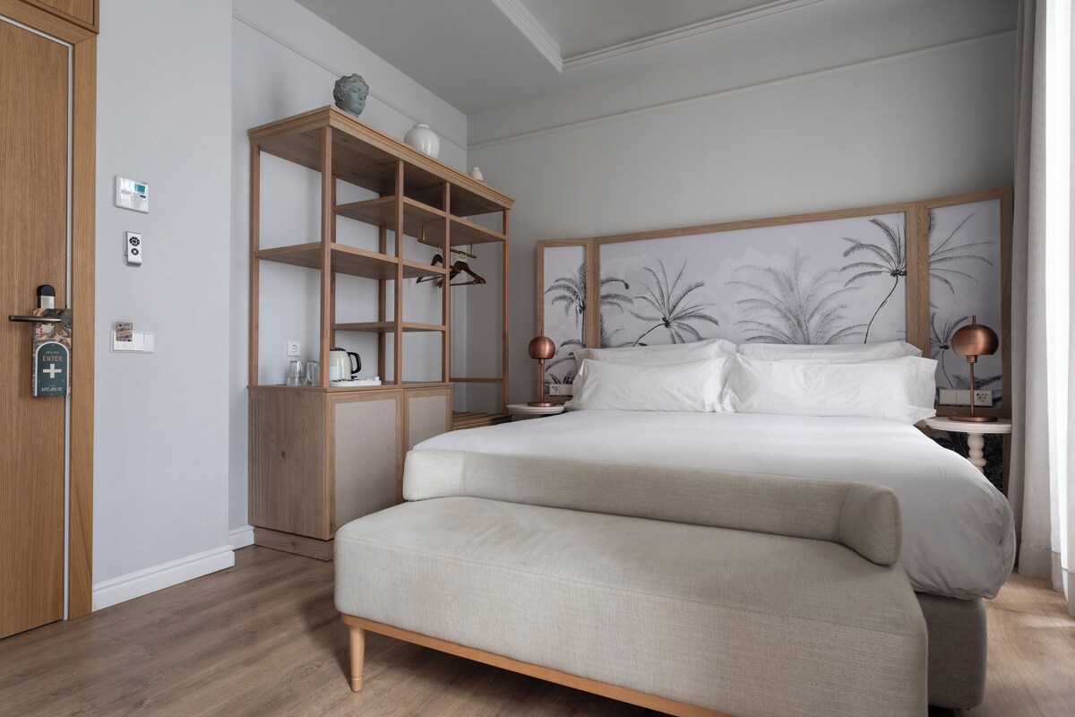 A bedroom with a large bed, a wooden wardrobe, a bedside table with a lamp, and a wall-mounted shelf.