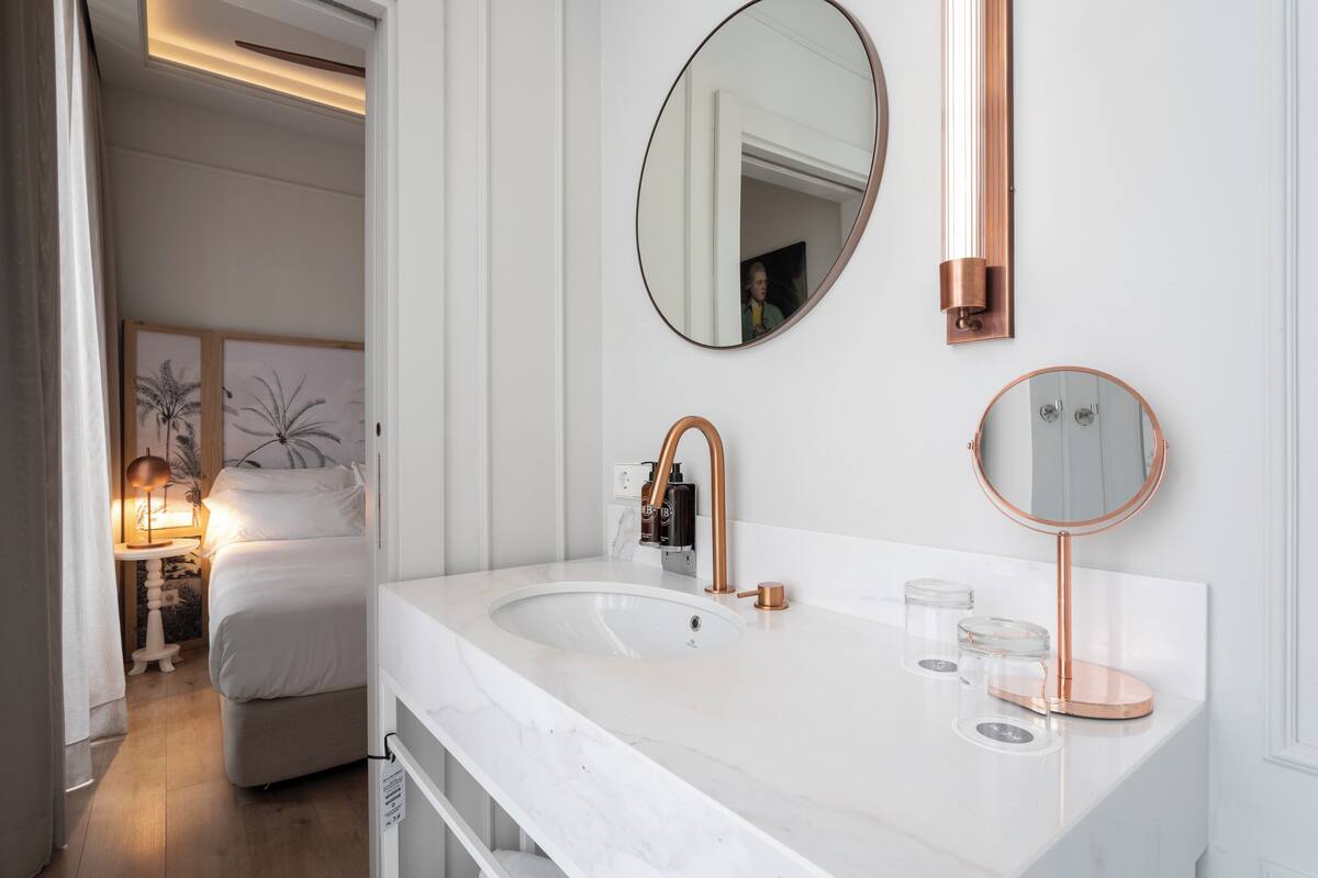 A modern bathroom with a white marble sink, copper fixtures, and a large mirror.