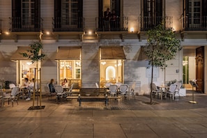 An outdoor café area with tables and chairs, a bench, and a small tree. - Malabar by Petit Palace Anteriormente Icon Malabar (Málaga)