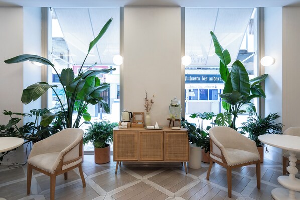 A room with a large window, a wooden cabinet, two beige chairs, and several potted plants. - Malabar by Petit Palace Anteriormente Icon Malabar (Málaga)