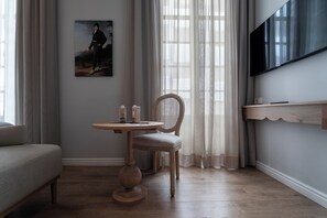 A room with a wooden floor, a round table with a chair, a sofa, a painting on the wall, and a TV mounted on the wall. - Malabar by Petit Palace Anteriormente Icon Malabar (Málaga)