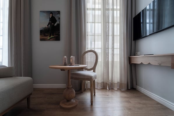 A room with a wooden floor, a round table with a chair, a sofa, a painting on the wall, and a TV mounted on the wall. - Malabar by Petit Palace Anteriormente Icon Malabar (Málaga)