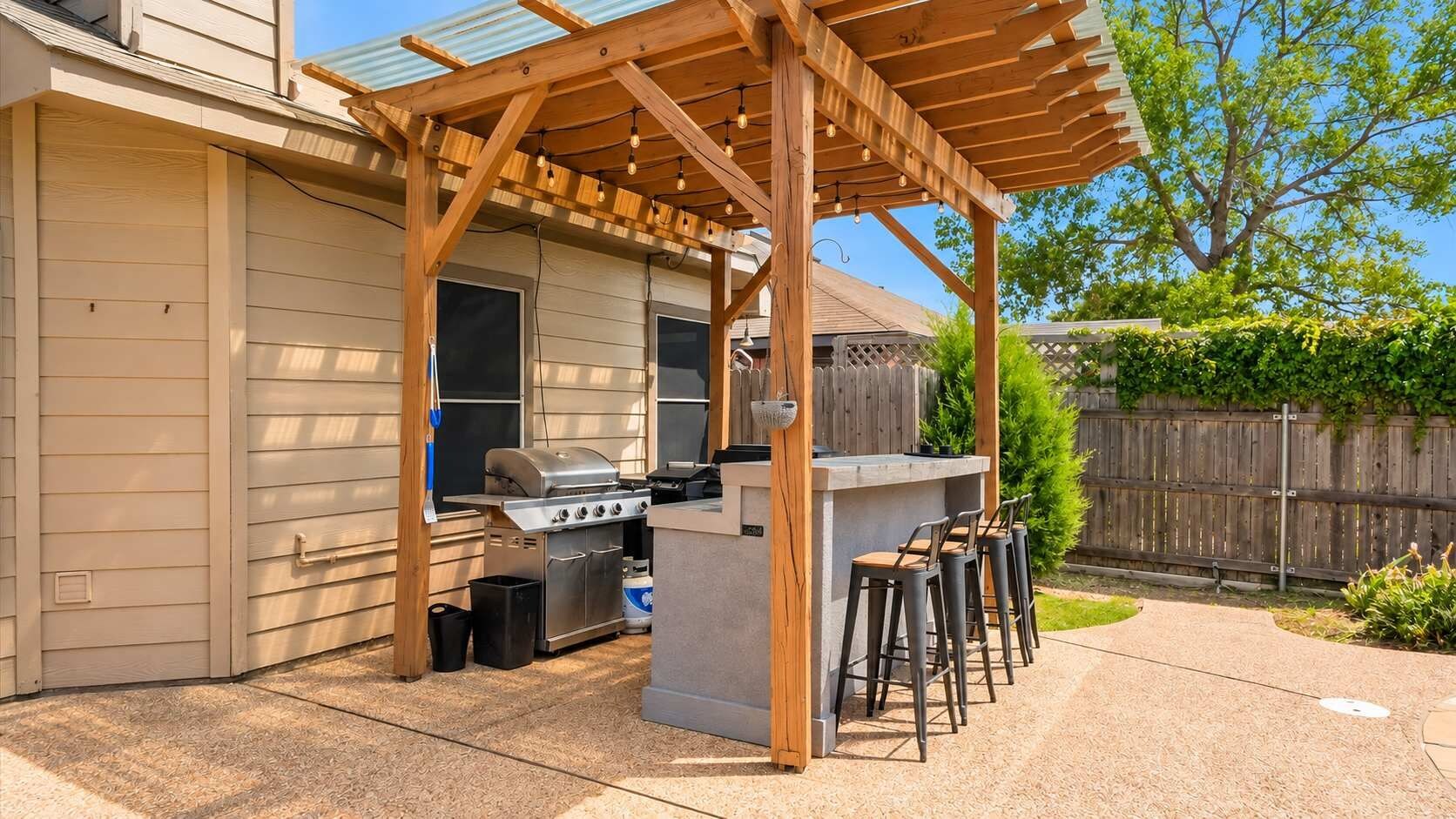 An outdoor kitchen area with a grill, bar stools, and a pergola structure.