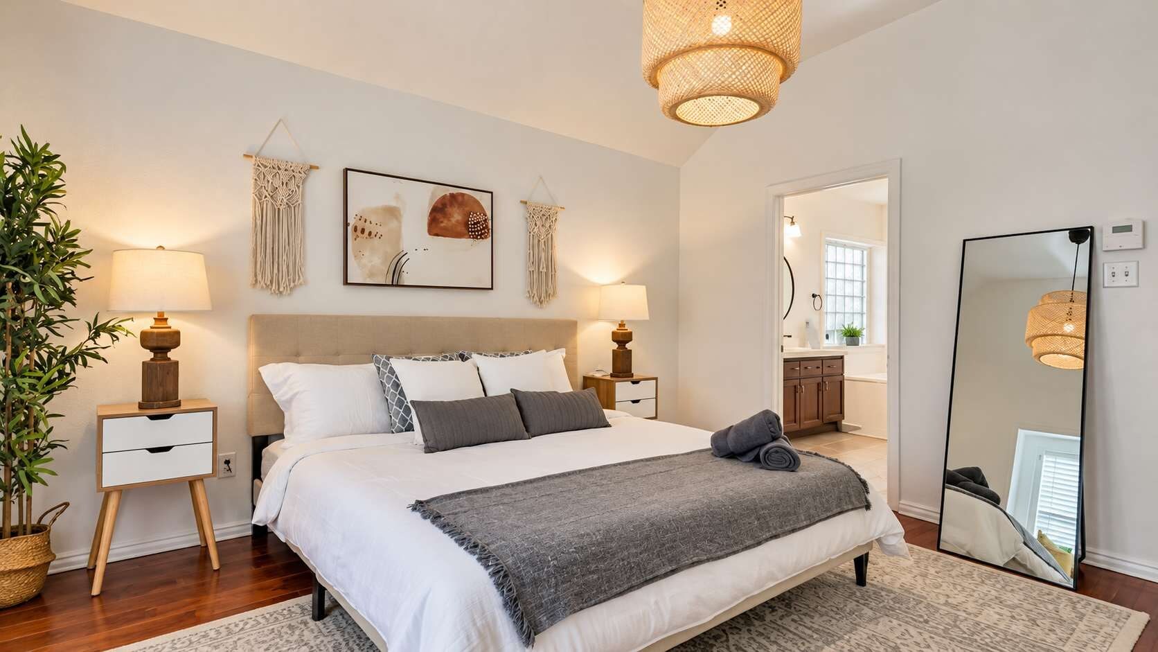 A bedroom with a bed, bedside tables, a mirror, and a potted plant.