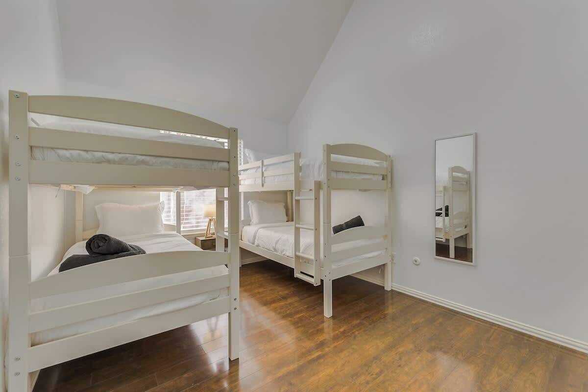 Um quarto com três beliches, um espelho na parede e piso de madeira.