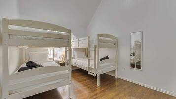 Um quarto com três beliches, um espelho na parede e piso de madeira.