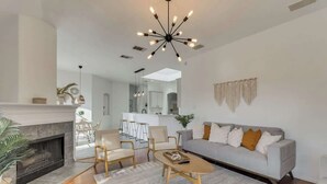 A modern living room with a fireplace, a sofa, a coffee table, and a dining area with chairs. - Elite 4BR/2B Home with Hot Tub, Pool, and BBQ (Haltom City)