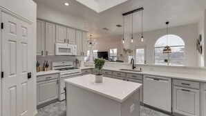 A modern kitchen with white cabinetry, a central island, and pendant lighting. - Elite 4BR/2B Home with Hot Tub, Pool, and BBQ (Haltom City)