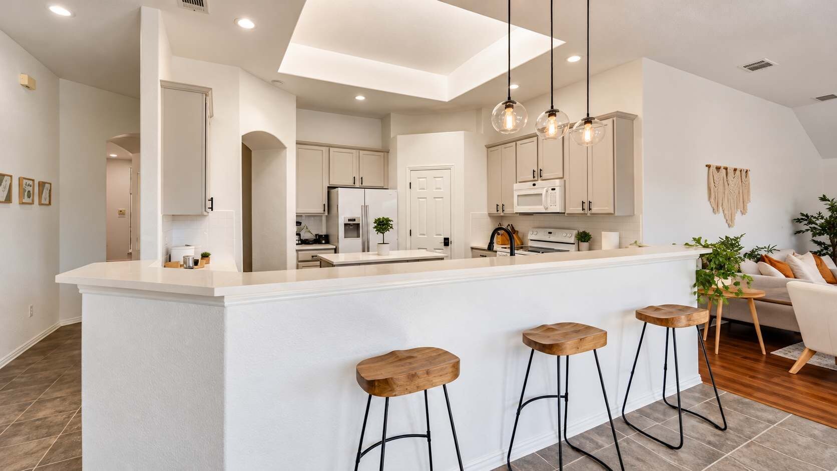 A modern kitchen with a central island, bar stools, and pendant lighting.