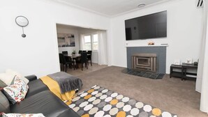 Ein modernes Wohnzimmer mit einer Couch, einem Kamin, einem Essbereich und einem an der Wand montierten Fernseher.