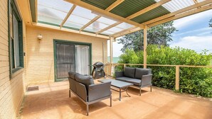 Eine überdachte Terrasse mit Gartenmöbeln, einem Grill und Blick auf Grünflächen.