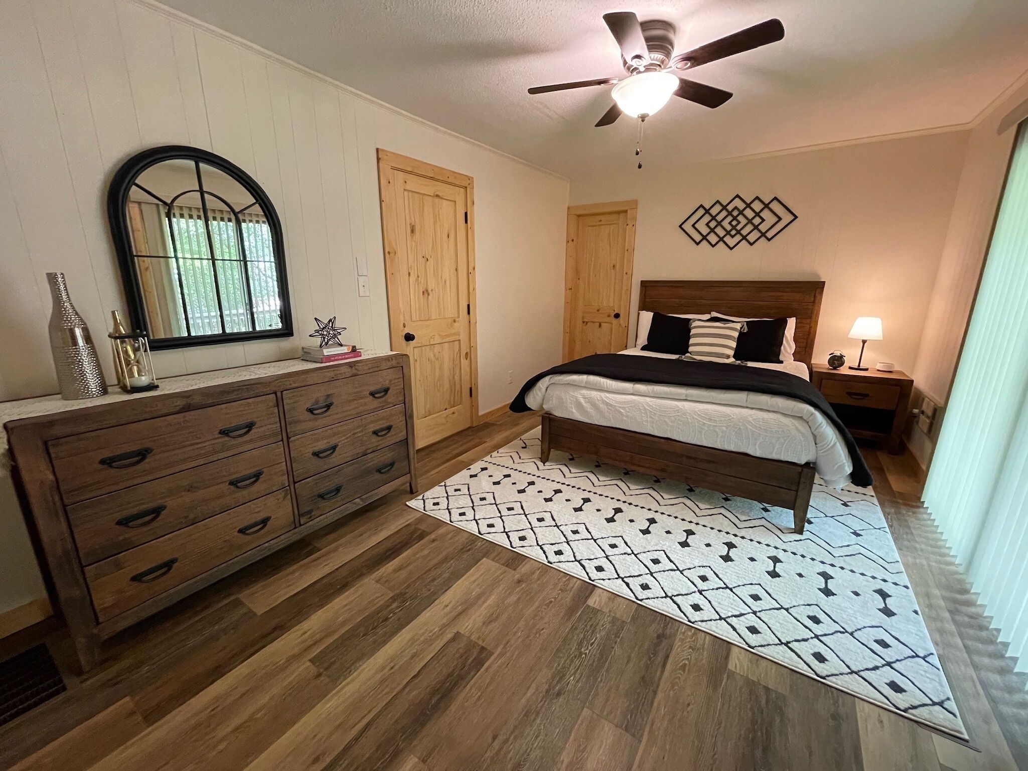 A bedroom with a wooden dresser, a bed with a headboard, a ceiling fan, and a patterned rug.