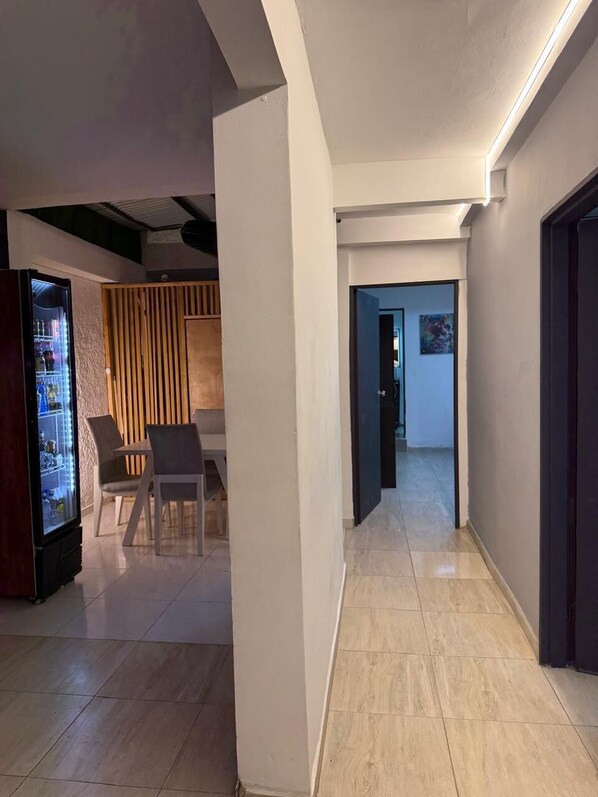 A hallway with a refrigerator, a dining area with chairs, and a door leading to another room.