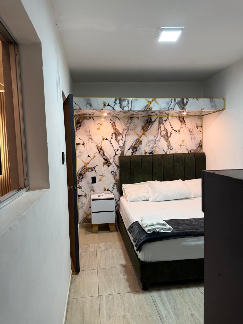 A bedroom with a bed, nightstand, and a wall with a marble-like pattern.