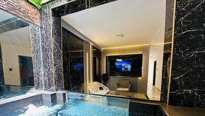 An indoor swimming pool with a waterfall feature, a lounge area with seating, and a modern interior design with marble walls. - house with jacuzzi near lleras park  (Medellin)