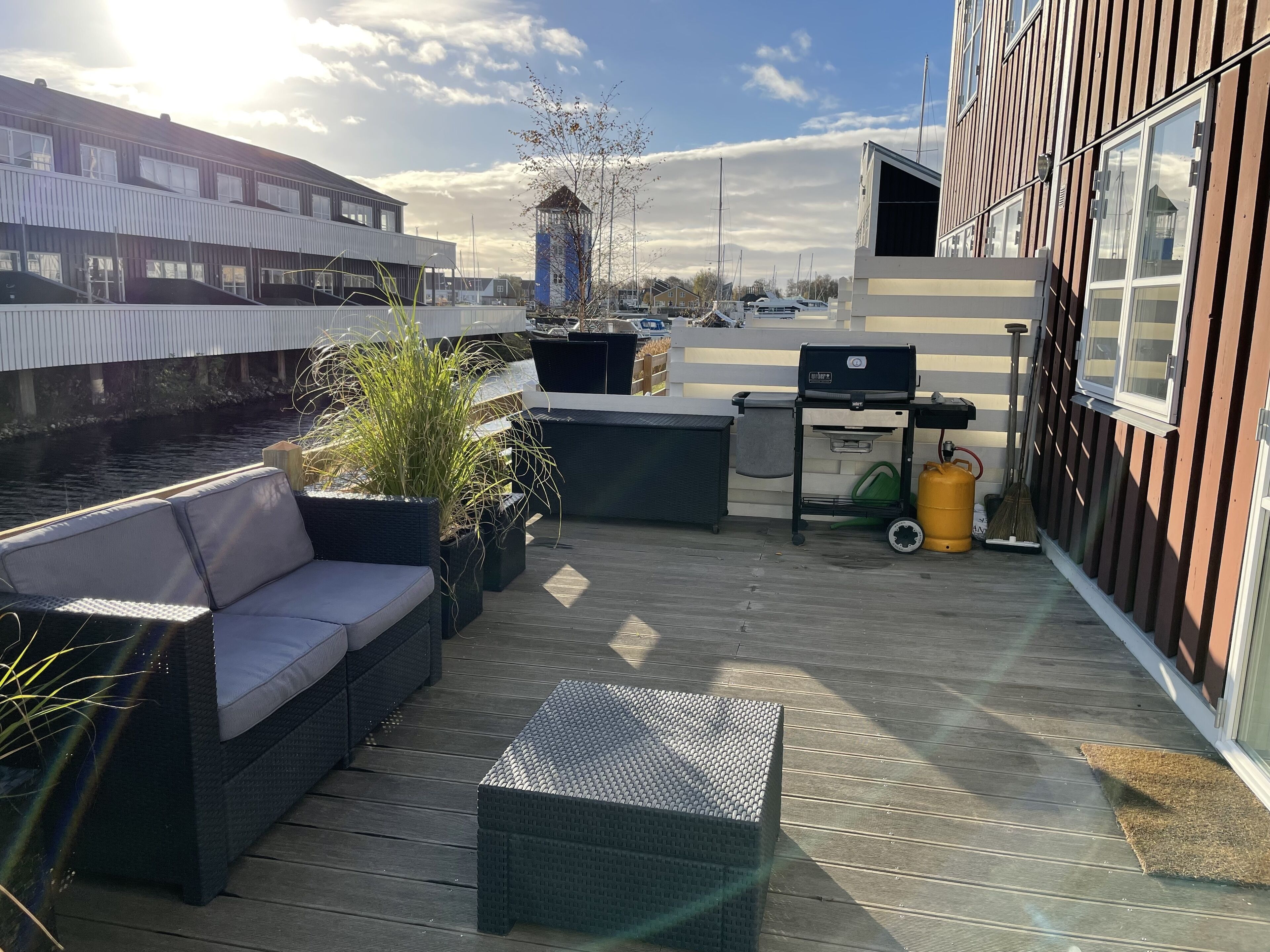 Une terrasse avec un canapé, des jardinières, un barbecue et une vue sur l’eau et les bâtiments en arrière-plan.