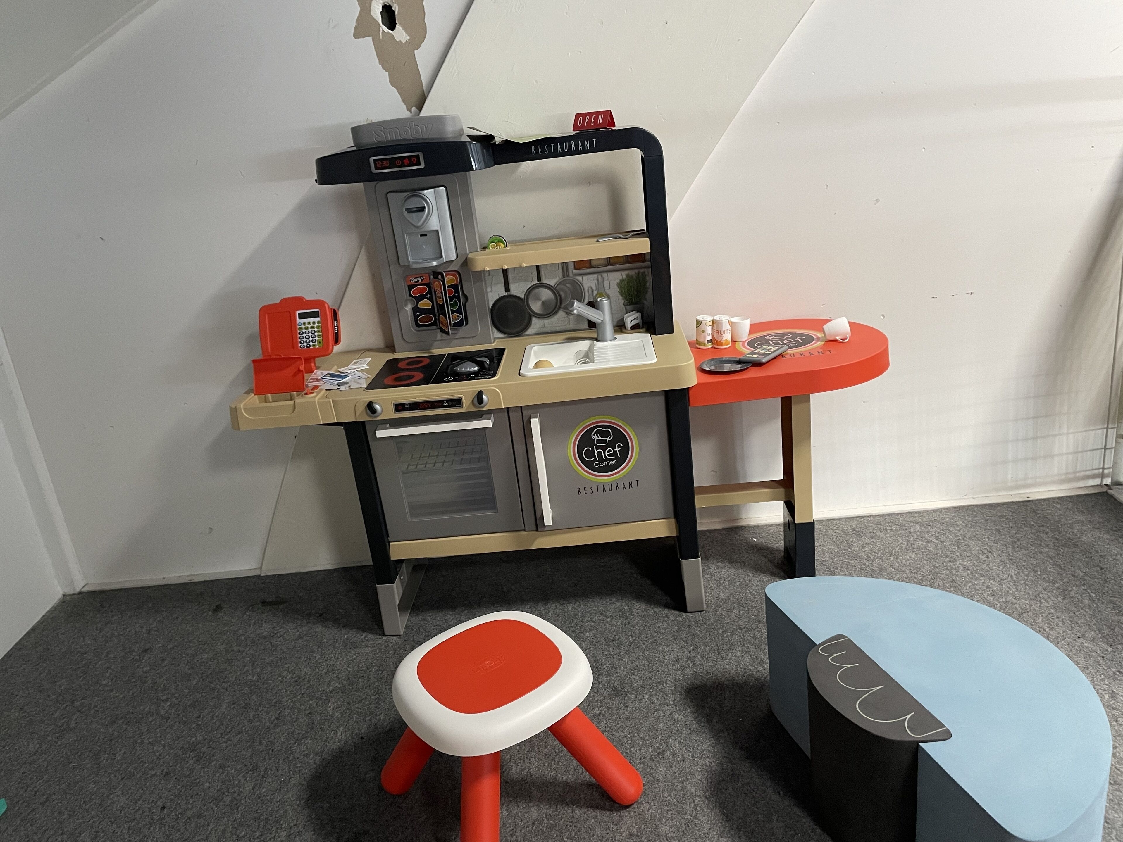 A play kitchen with a coffee machine, a sink, and a small table with cups and a spoon.