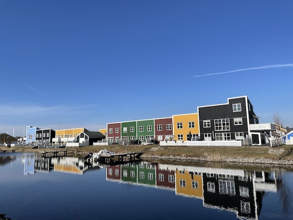 A row of colorful buildings along a calm water body, reflecting the structures. - Activitiesonsite - Nationalpark-7 Islands, Denmark (Ebeltoft)