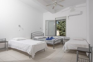 Une chambre avec deux lits, un ventilateur de plafond, une fenêtre donnant sur les arbres et un climatiseur fixé au mur.