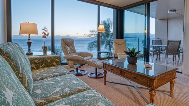 Habitación de hotel moderna con un balcón amplio, un escritorio de cristal y un sofá con vistas al océano.