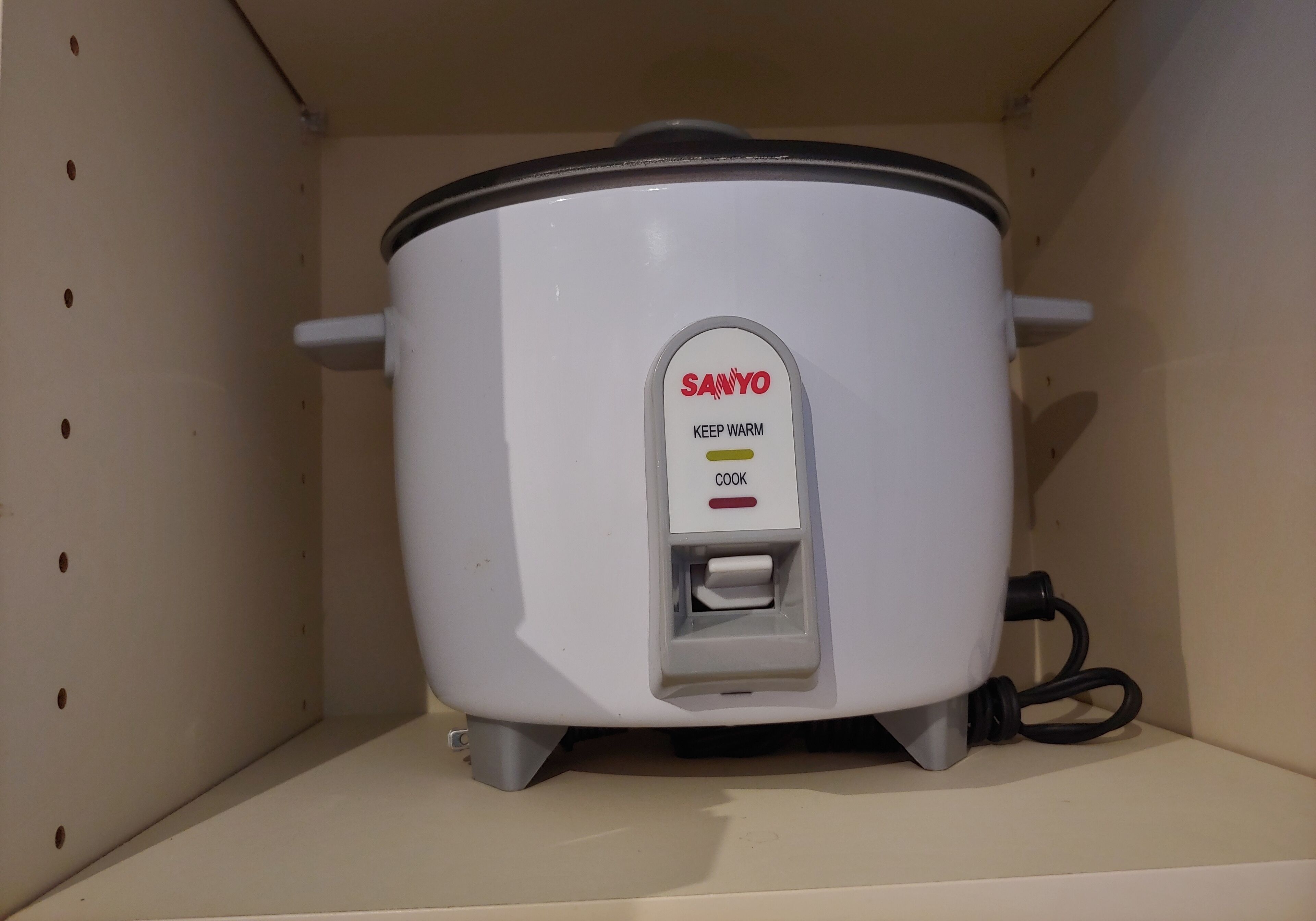 A white Sanyo slow cooker with a control panel, placed on a shelf.