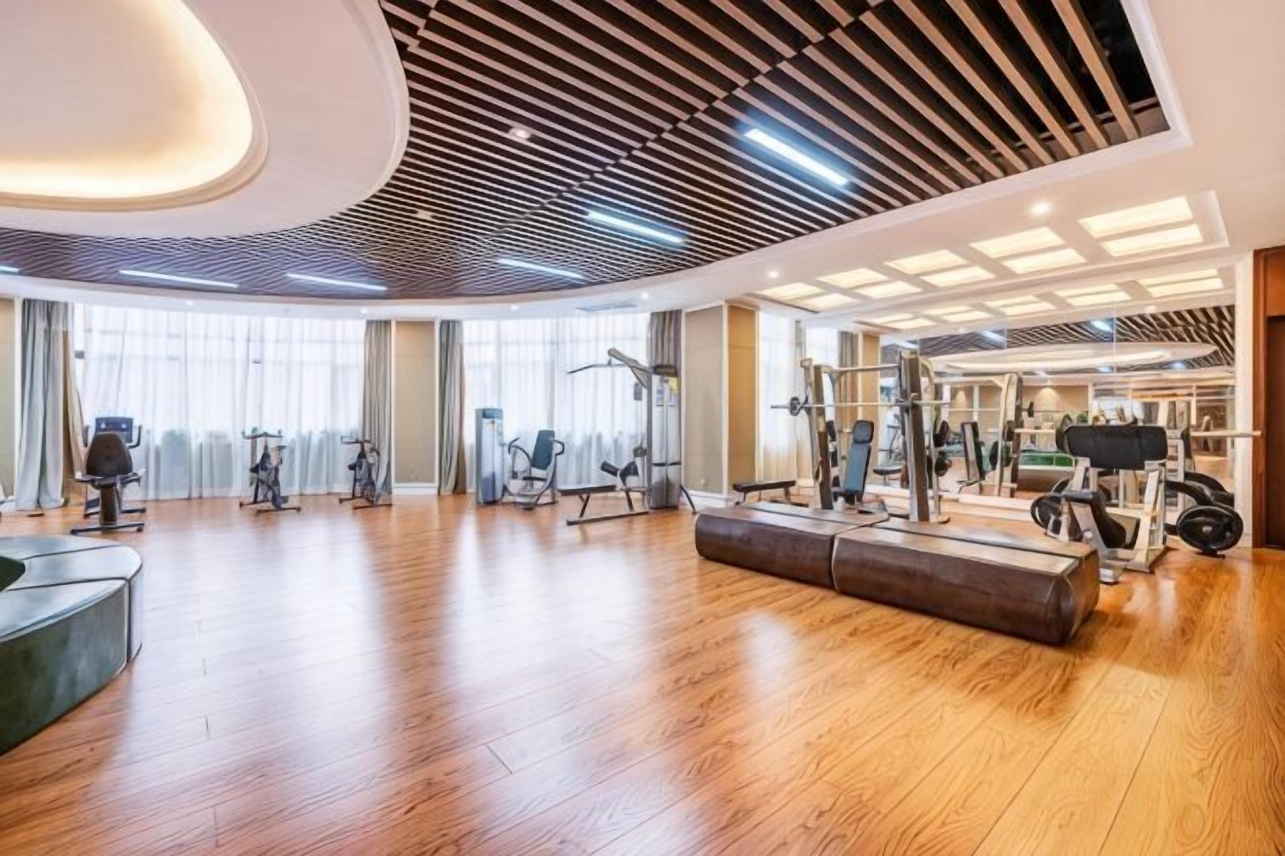Ein geräumiger Fitnessraum mit Holzböden, Trainingsgeräten und großen Fenstern.