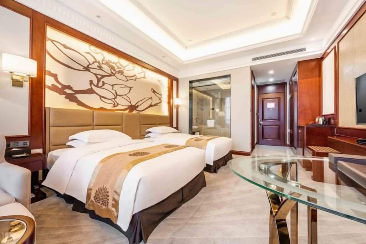 A hotel room with two beds, a glass dining table, a TV, and a decorative wall panel.