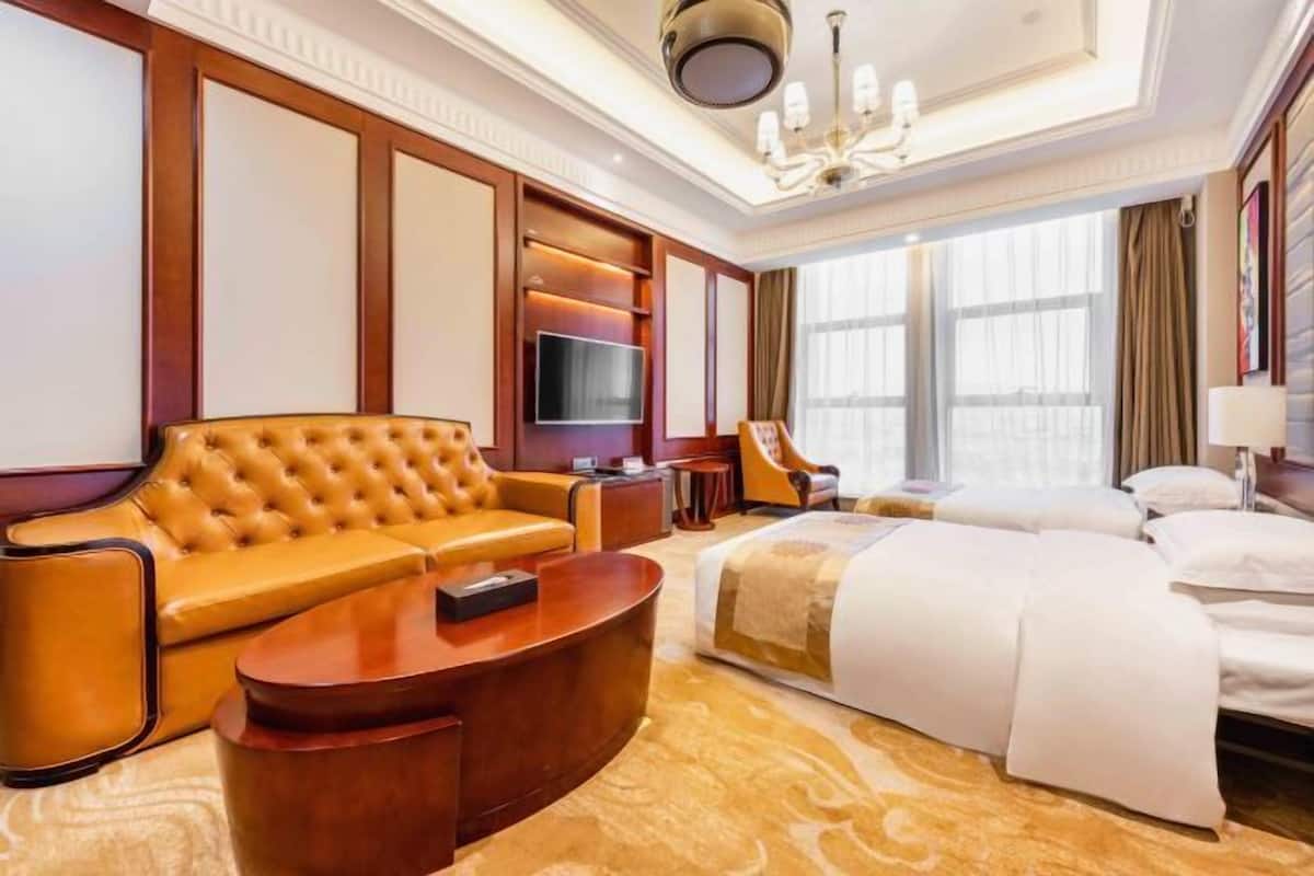 A spacious hotel room with a large bed, a leather sofa, a wooden coffee table, and a TV.