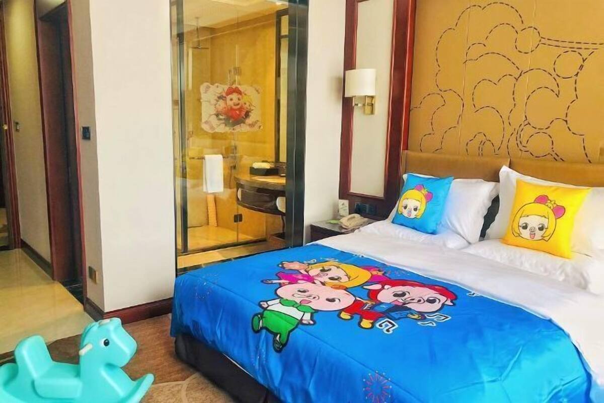 A hotel room with a bed featuring cartoon characters, a glass door leading to a bathroom, and a bear-themed headboard.