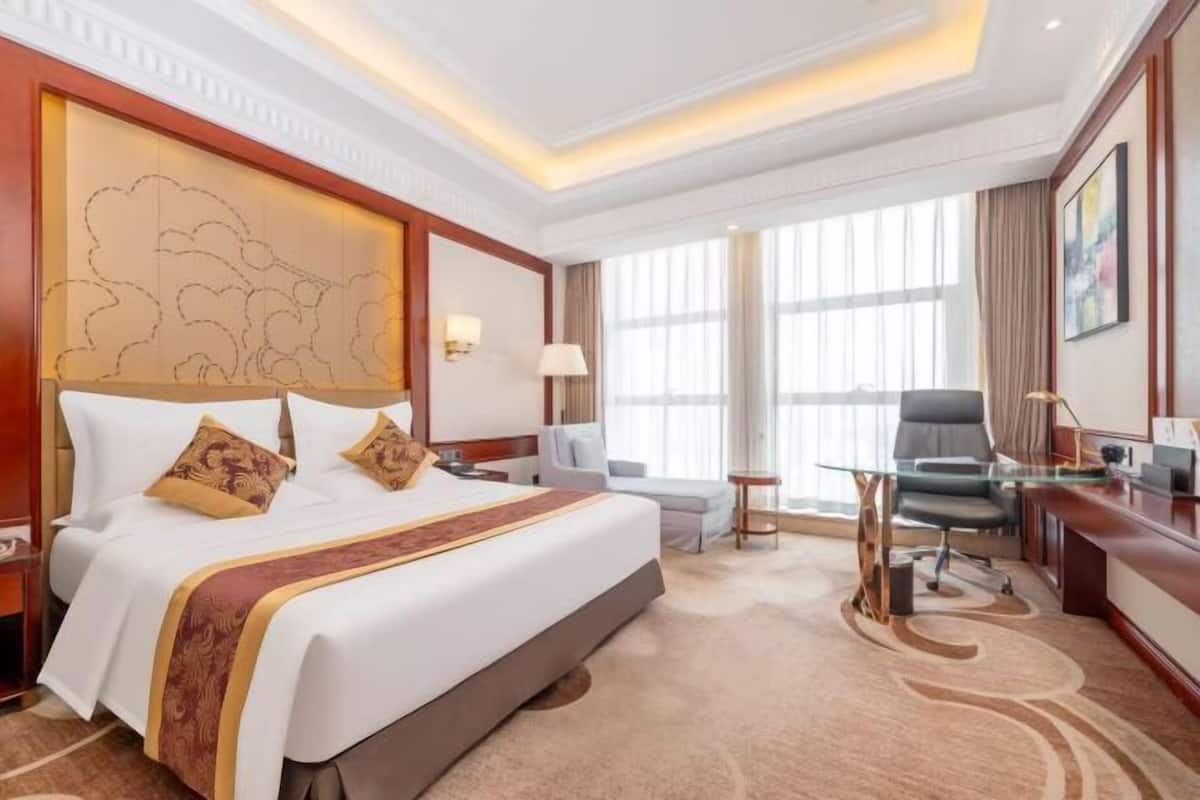 A hotel room with a large bed, a desk, a chair, and a large window.